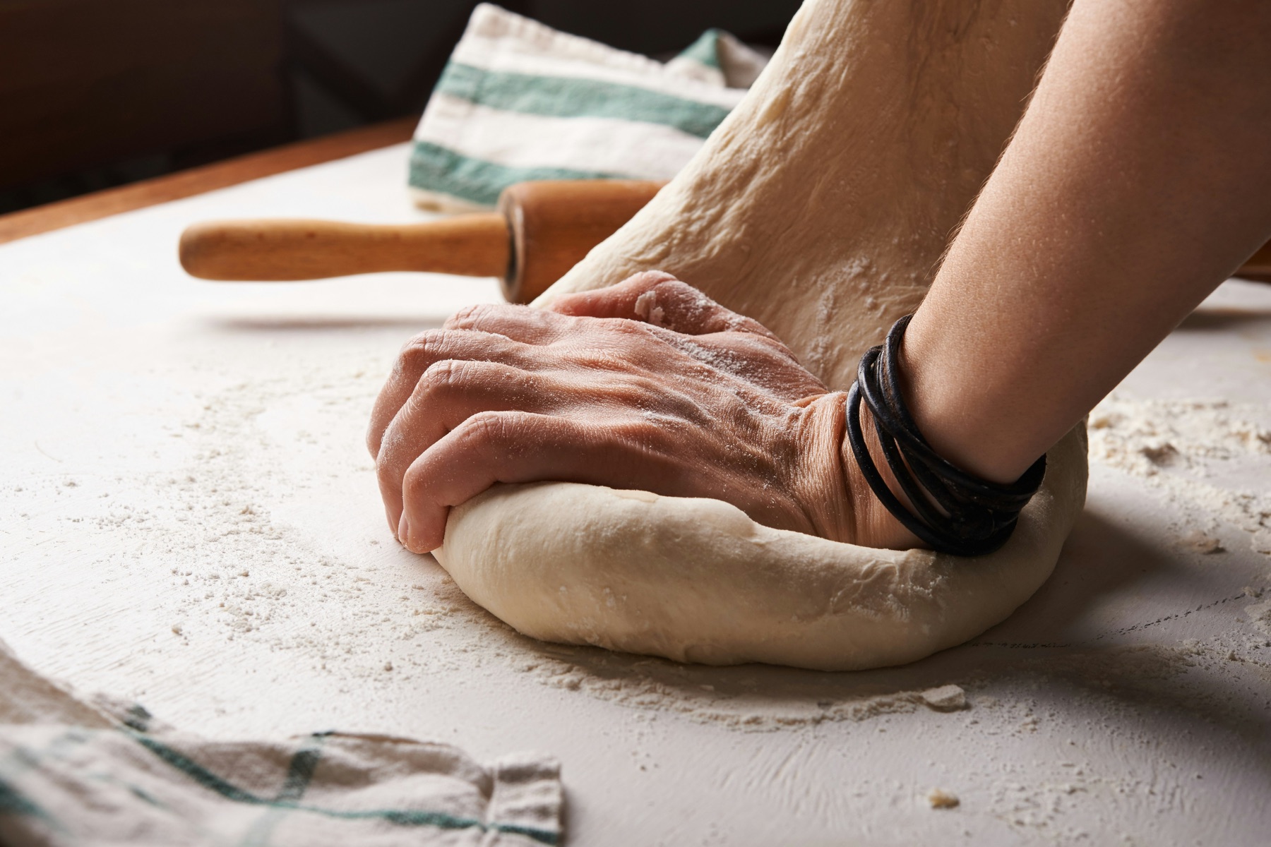 Pizza dough being stretched by hand on a floured surface