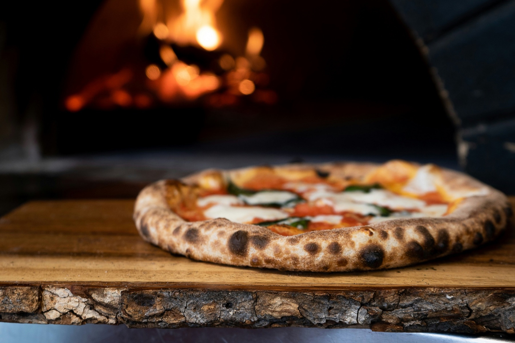 Fresh pizza beside the flames of a wood-fired oven